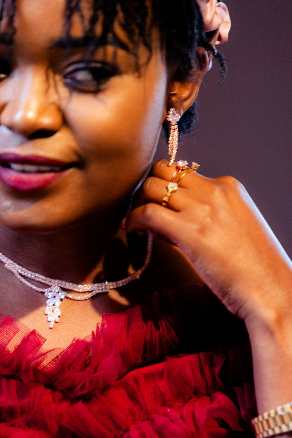 Woman in a red gown adjusts her sparkling earring.