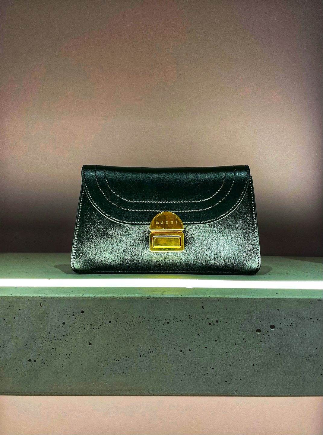 A dark leather handbag with a gold clasp on a concrete ledge.