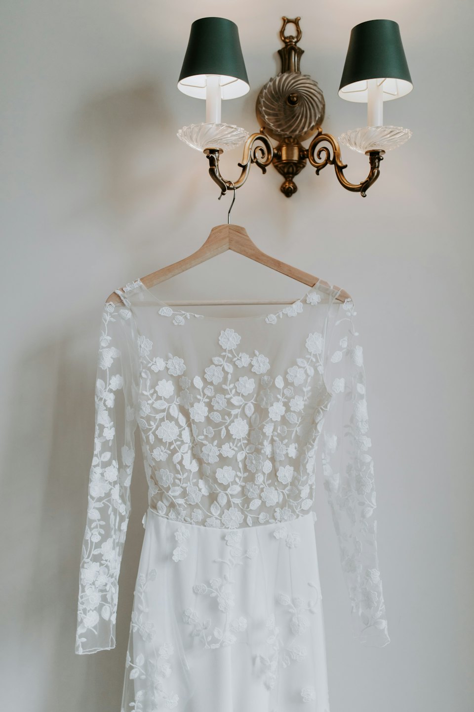 A white lace wedding dress hangs from a wooden hanger.